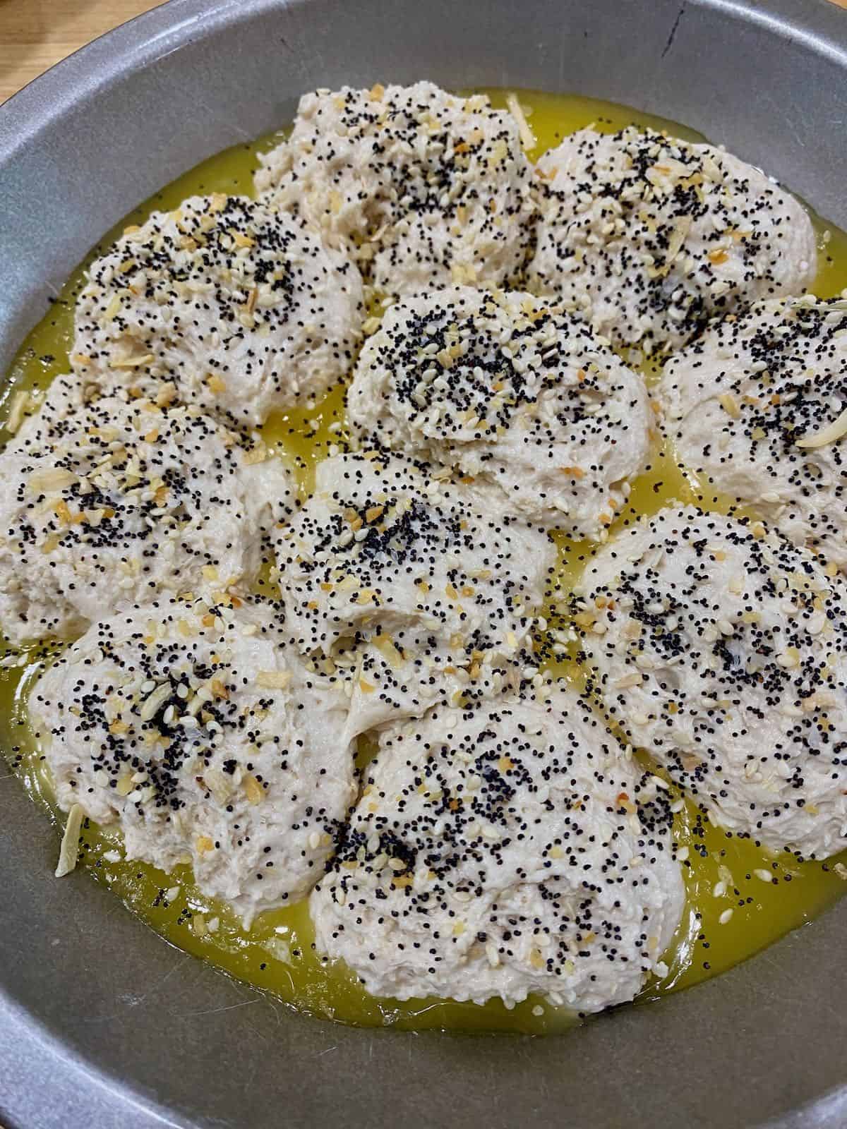 Unbaked biscuits in pan with butter and everything bagel topping.