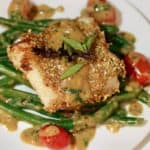 Roasted sesame cod on a plate with green beans, cherry tomatoes and lemon grass basil sauce.