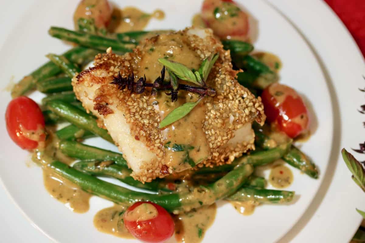 Roasted sesame cod on a plate with green beans, cherry tomatoes and lemon grass basil sauce.