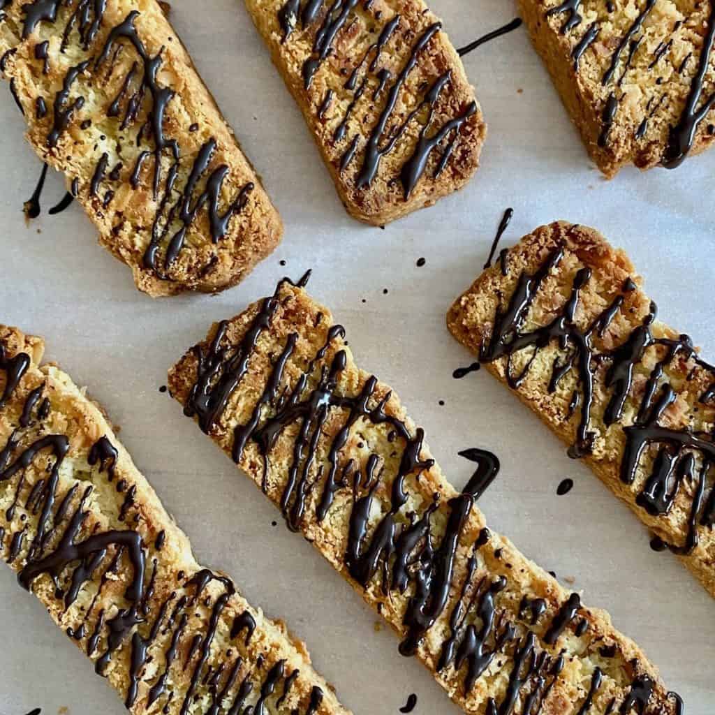 Espresso chocolate drizzled coconut biscotti on parchment paper.