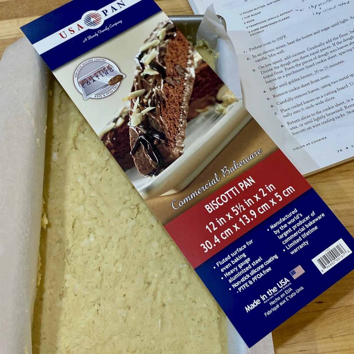 Ready to bake cookie batter in pan with biscotti pan information label and recipe book in background.