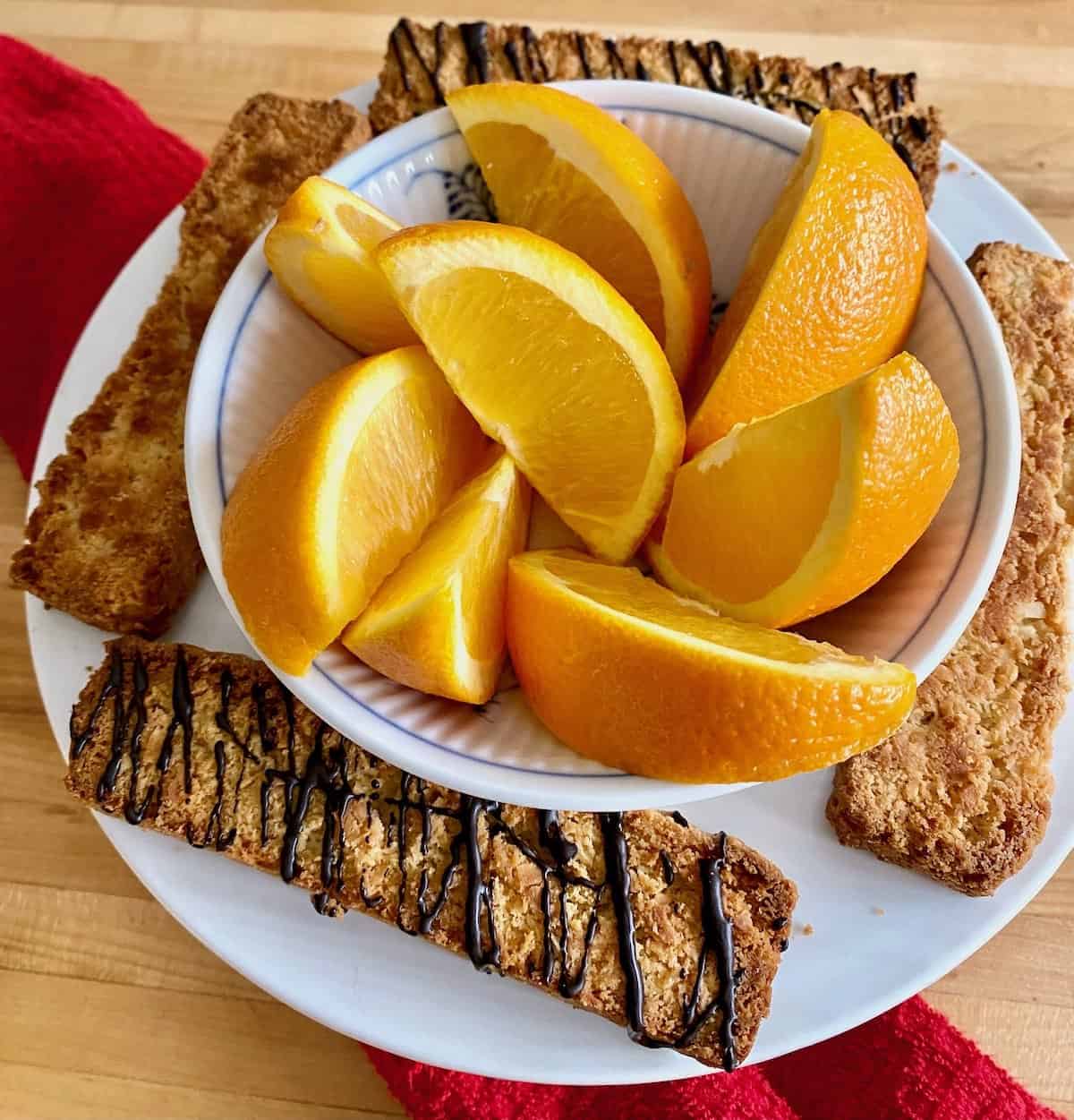 Toasted coconut biscotti with chocolate espresso drizzle on plate with oranges.