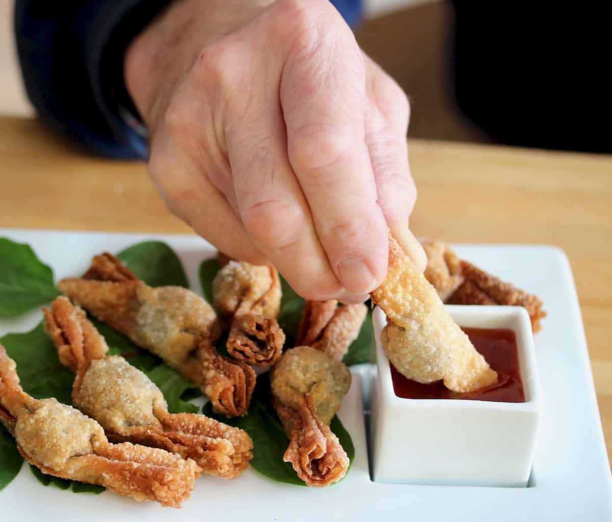 Hand holding wonton and dipping in sauce.