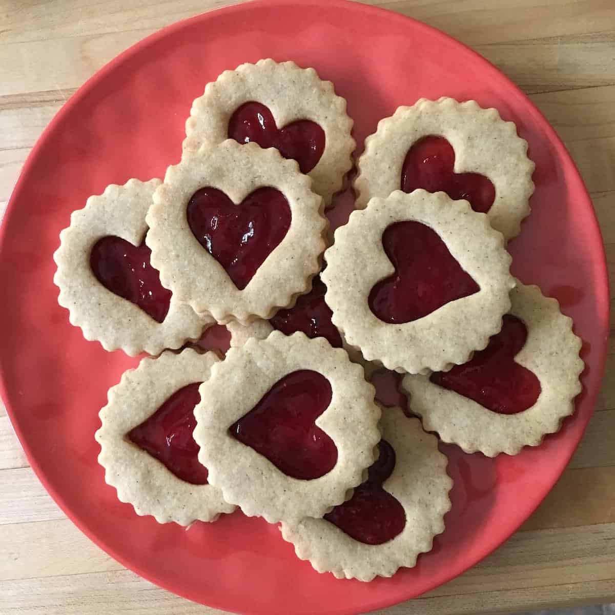 Plated linzer heart cookies on coral plate.