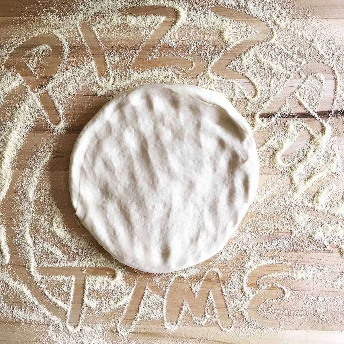 Pizza time written on cornmeal board with some pizza dough.