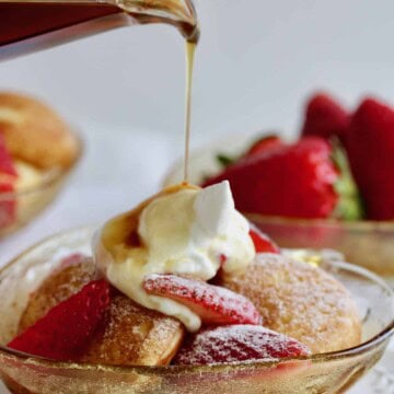 Strawberry stuffed pancakes in bowl with sliced strawberries, cream and syrup poured on top.