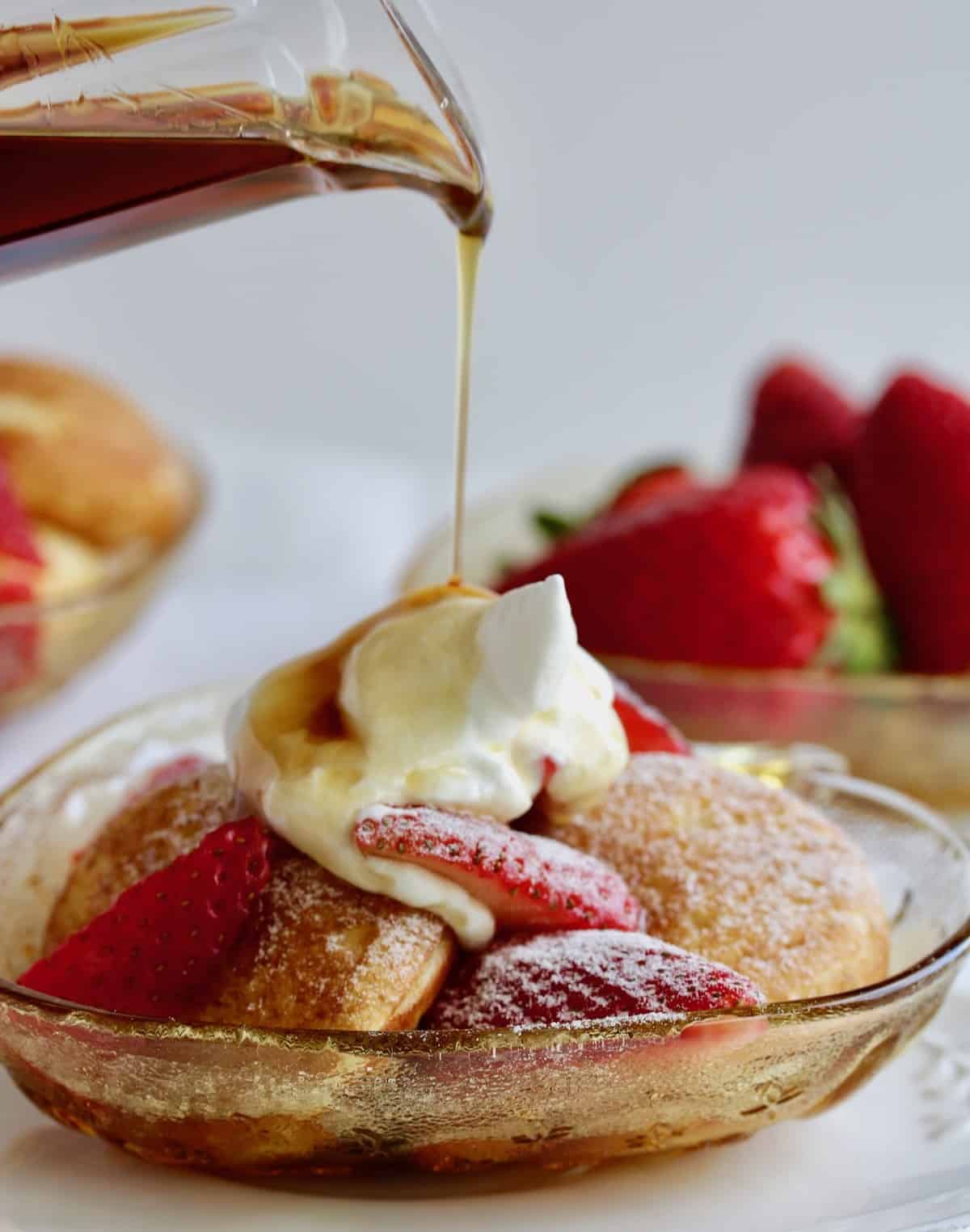 Strawberry stuffed pancakes in bowl with sliced strawberries, cream and syrup poured on top.
