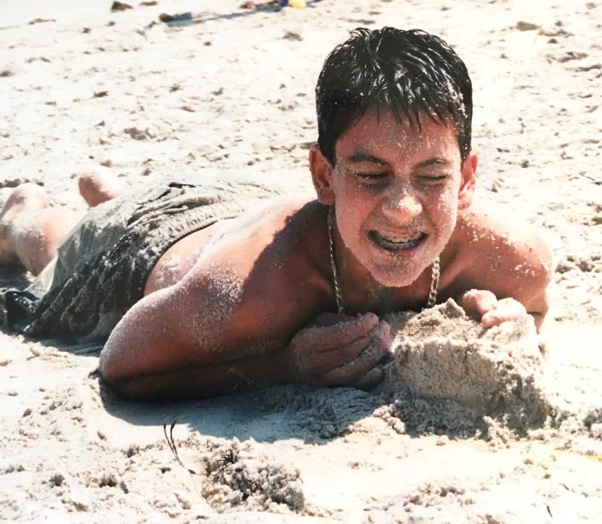 My young son at the beach covered in sand.
