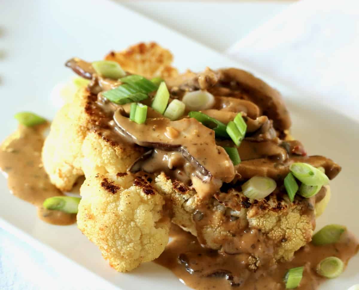 Plated cauliflower steak with lemon grass basil mushroom and green onion sauce.