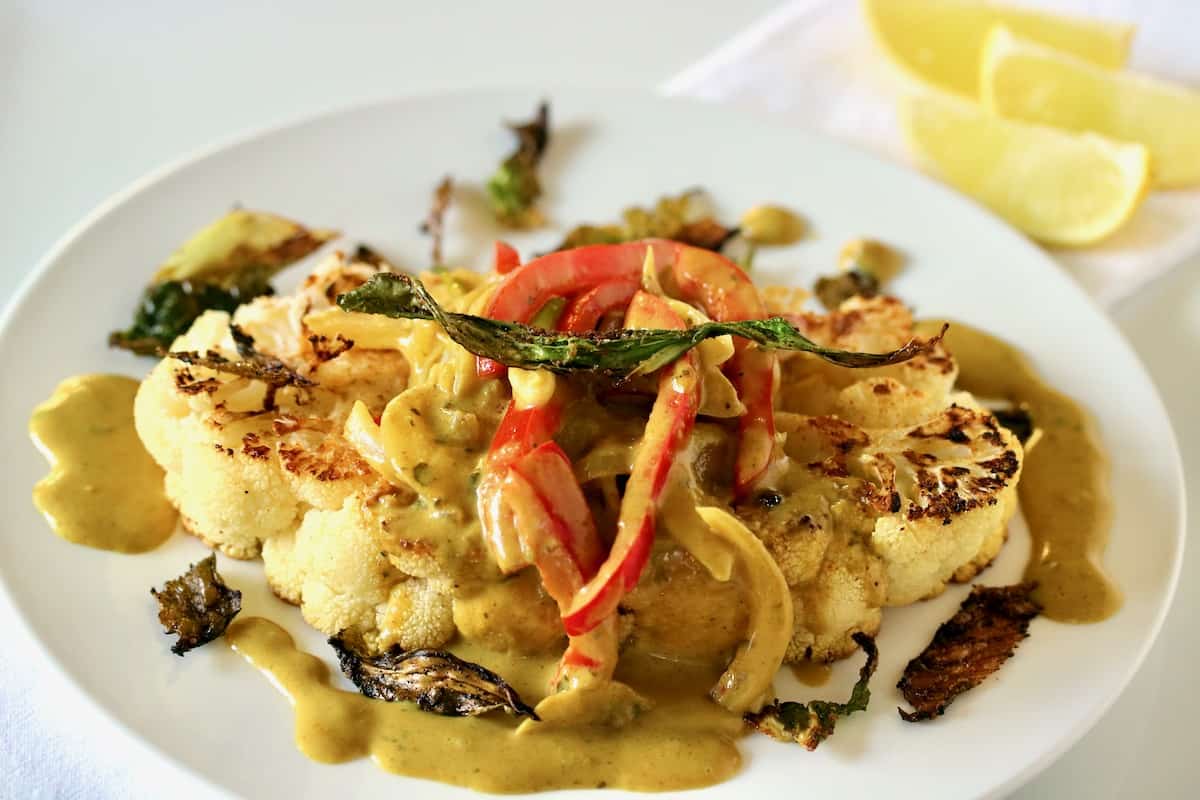 Plated cauliflower steak with peppers and onions Thai coconut sauce.