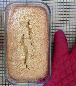 Coconut loaf cake on cooling rack with red potholder.