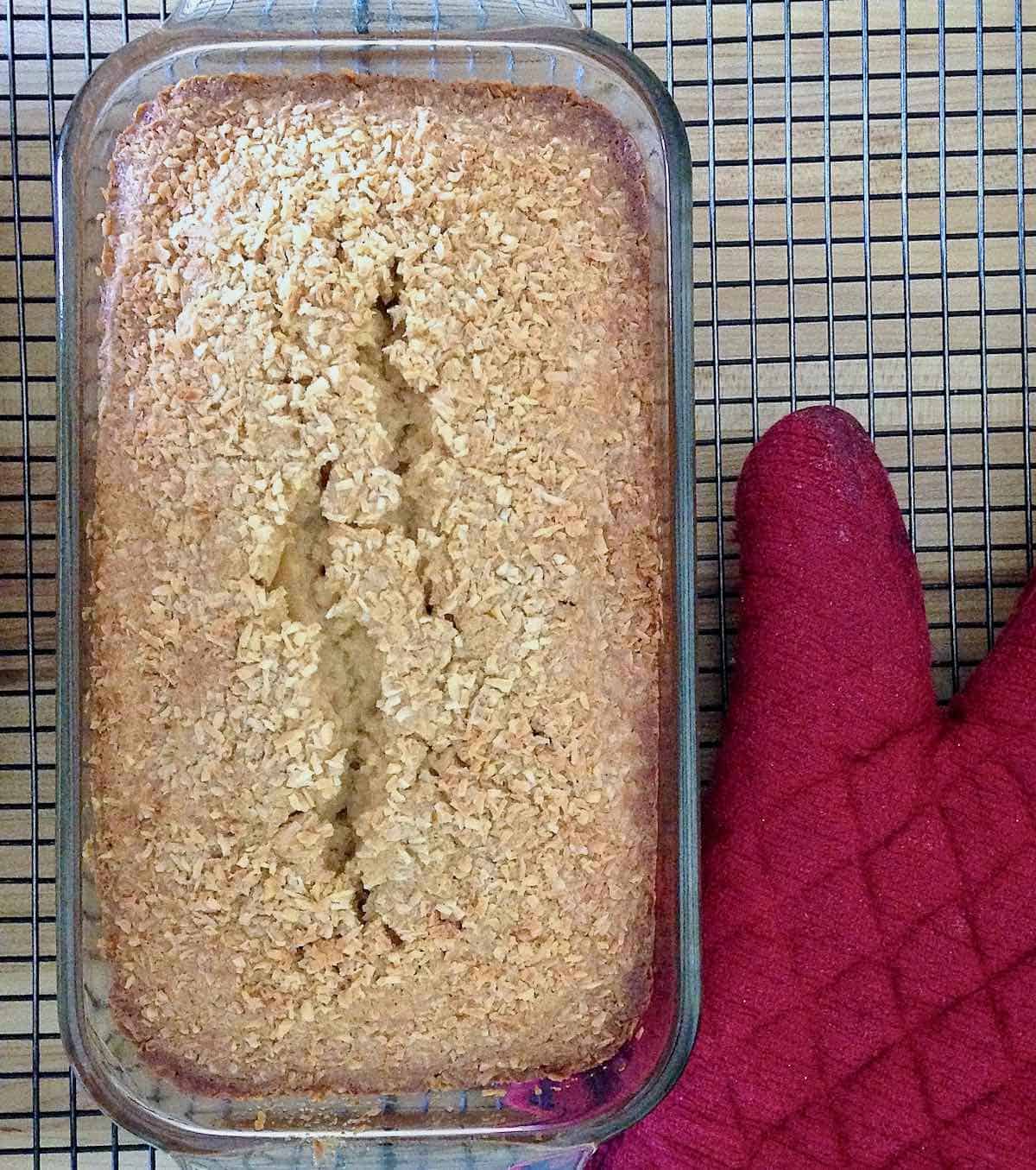 Coconut loaf cake on cooling rack with red potholder.