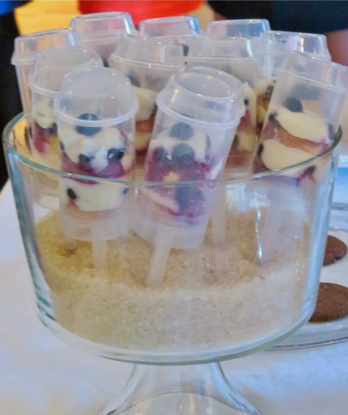 Berry mascarpone push up pops standing in a trifle bowl filled with rice.