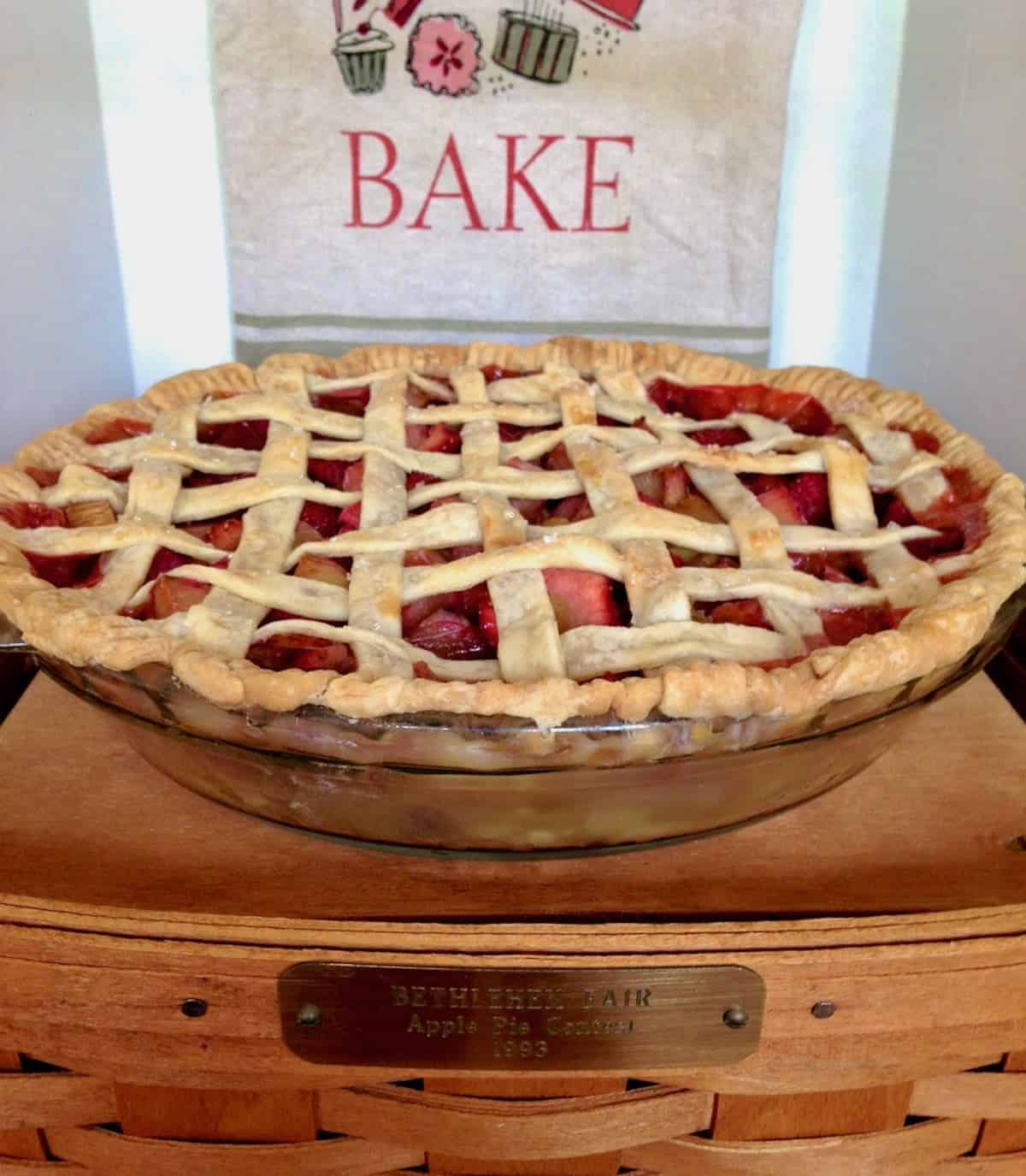 Strawberry rhubarb pie sitting on a basket with a tea towel that says BAKE.