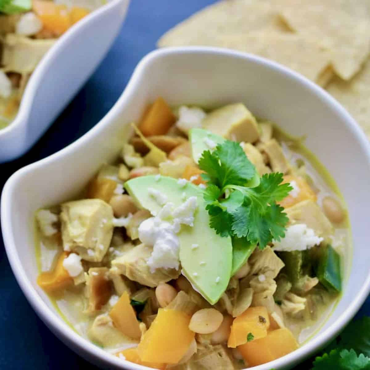Bowl of Thai chicken chili topped with avocado and tortillas.