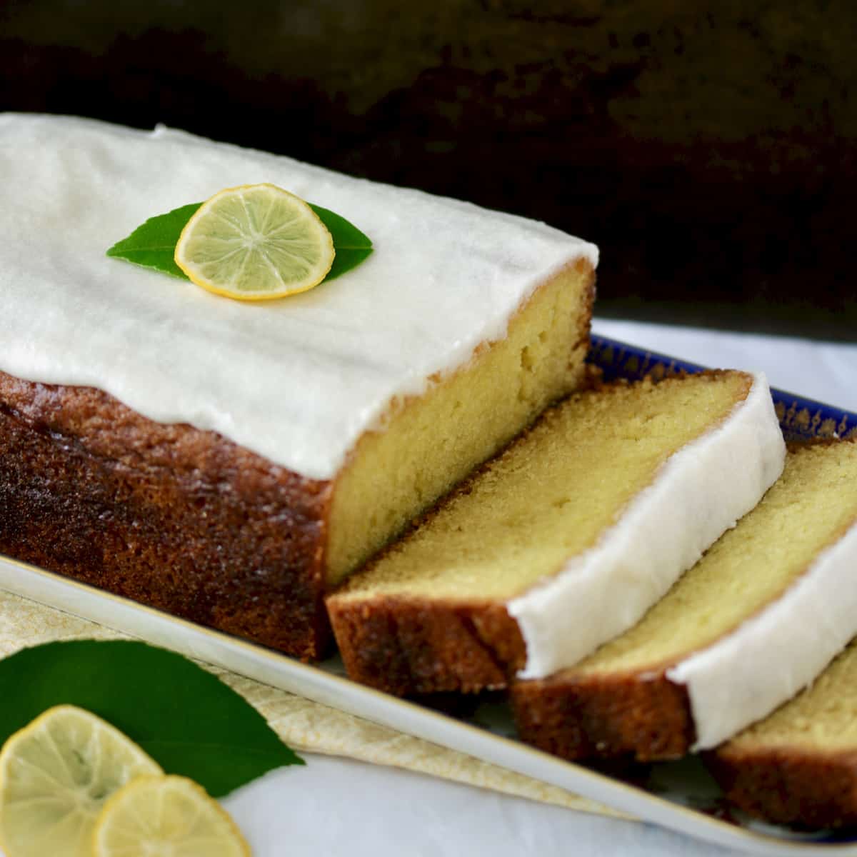 Sliced lemon loaf with white icing and lemon slice garnish.