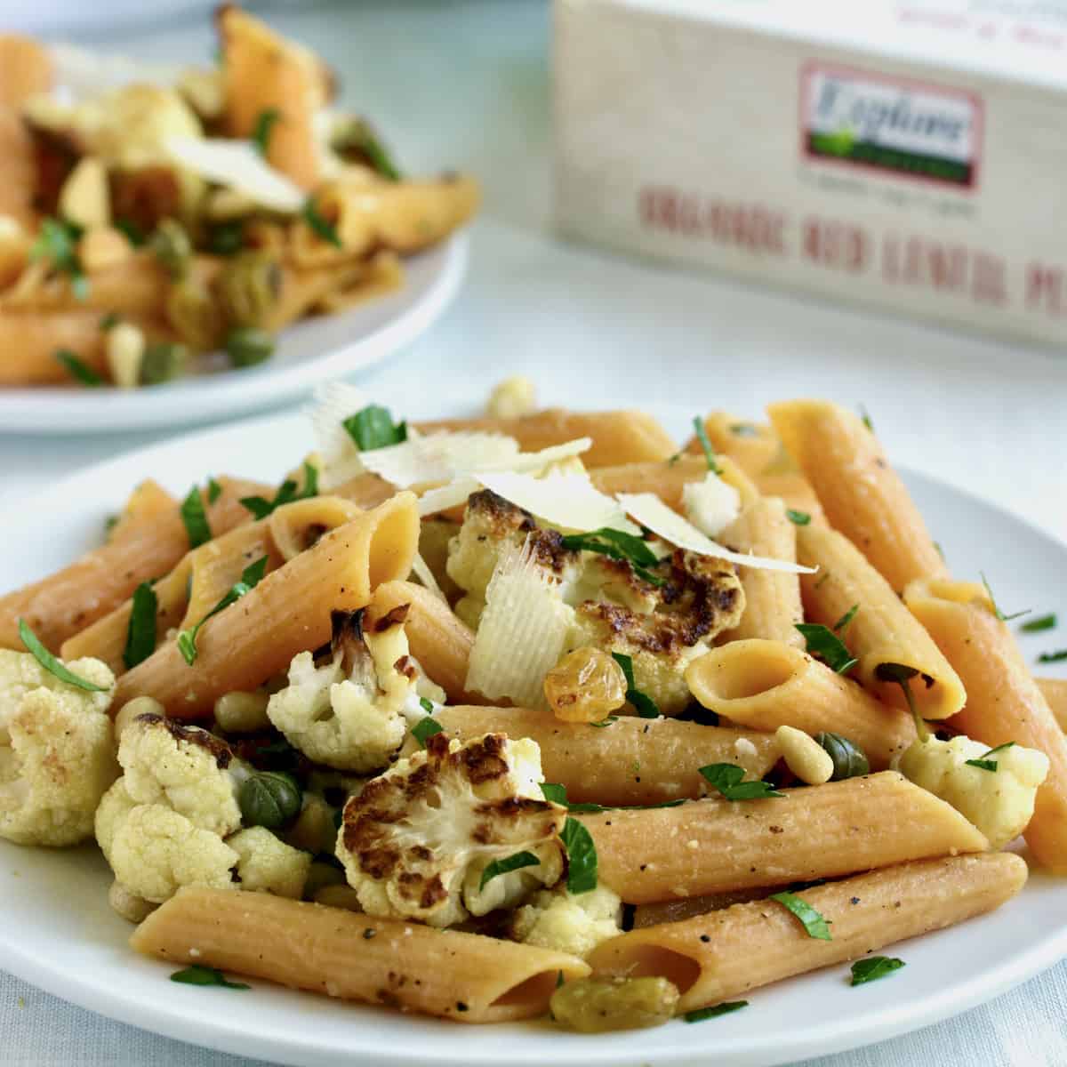 Plates of penne pasta with cauliflower, herbs and product package.