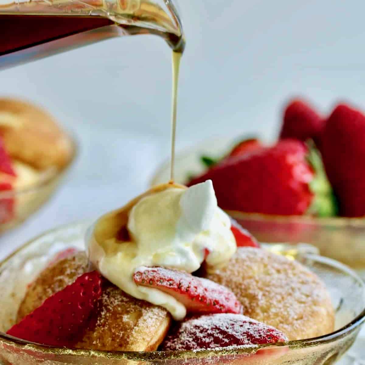 Strawberry stuffed pancakes in bowl with sliced strawberries, cream and syrup poured on top.