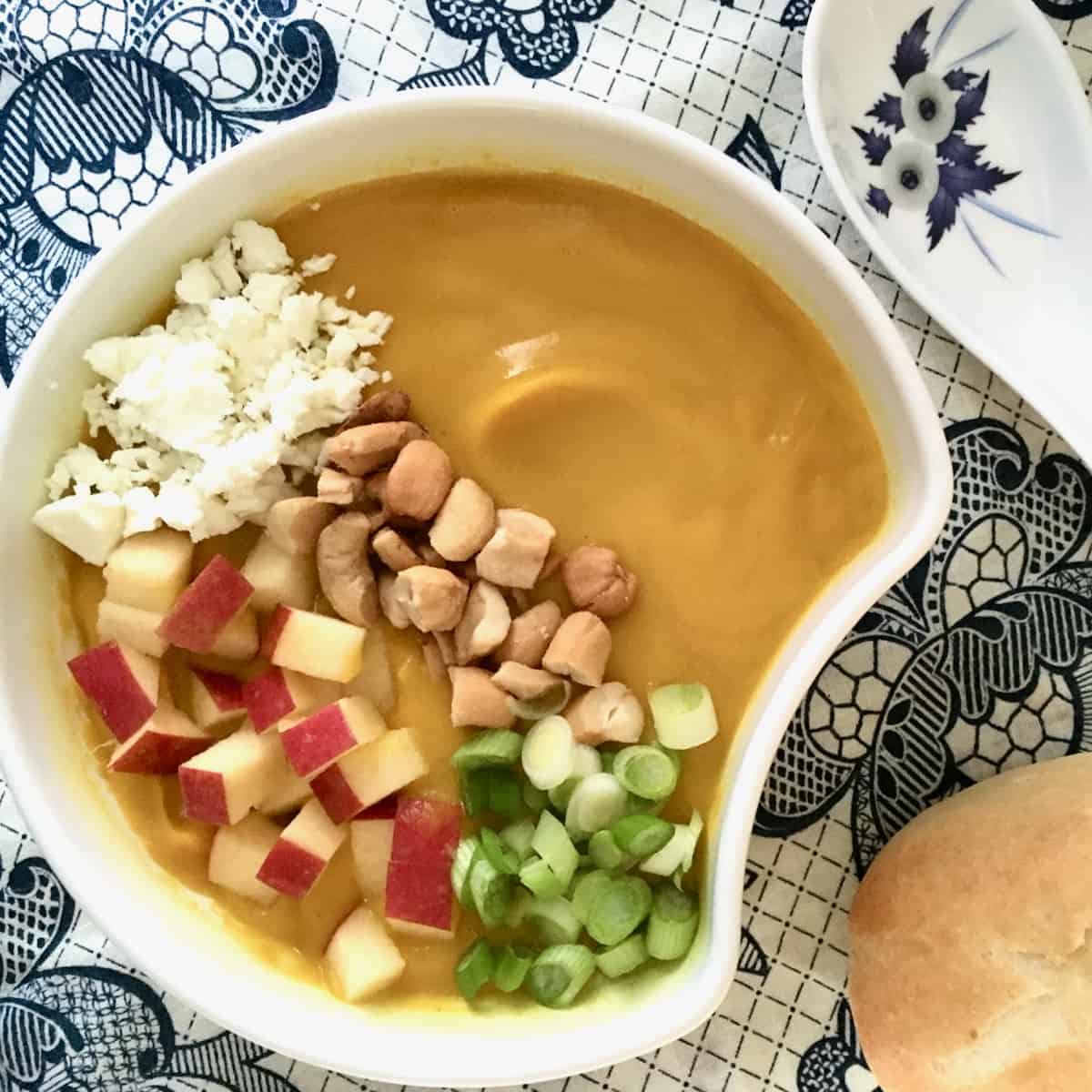 Bowl of soup topped with apples, cashews, green onions and cheese.