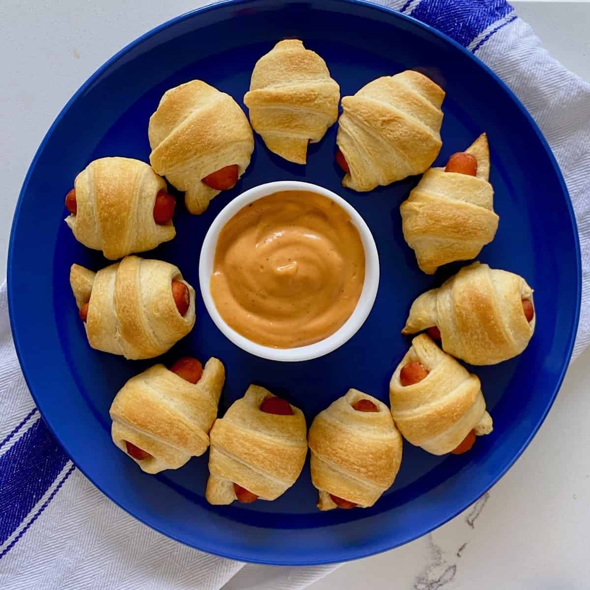 baby pigs in a blanket on blue plate with dipping sauce.