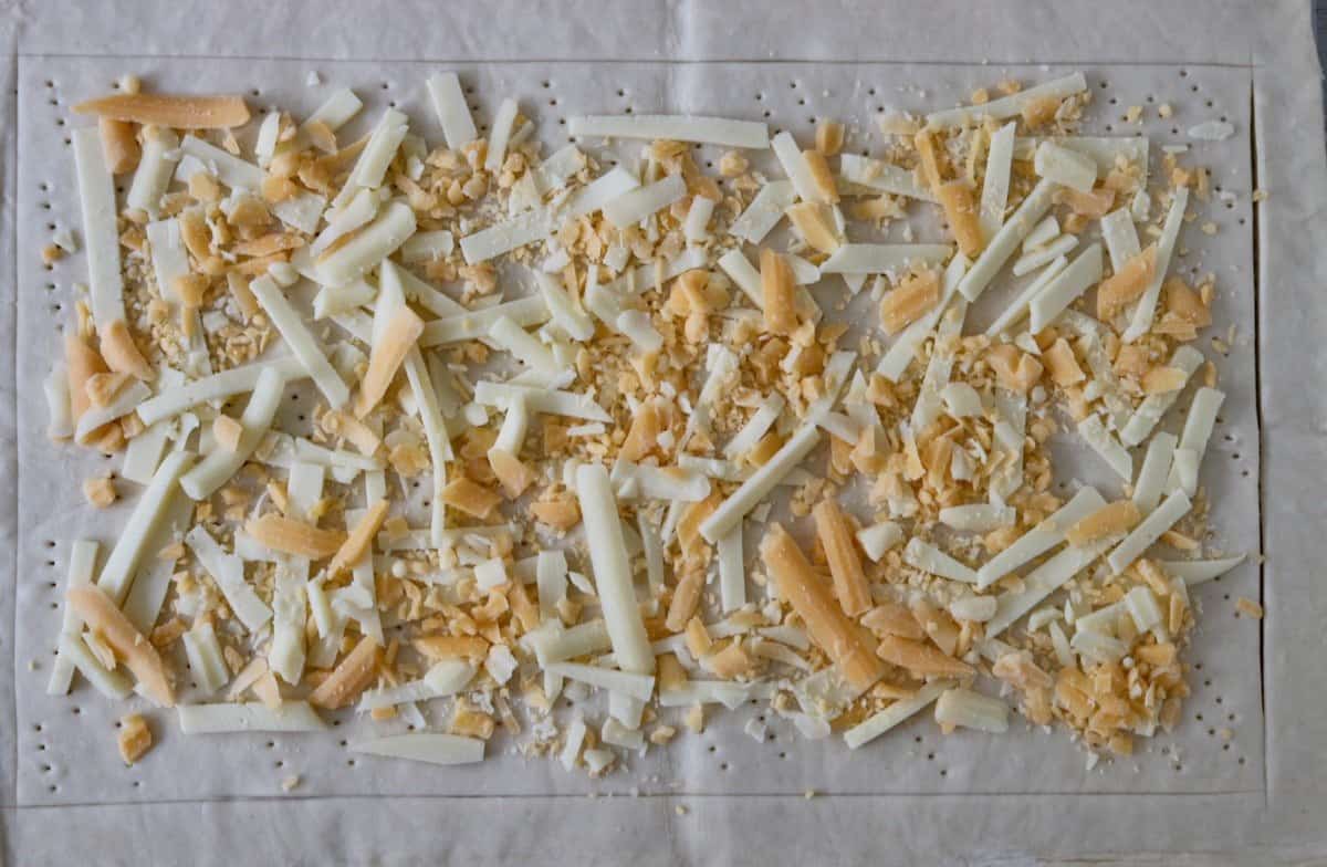 Unbaked docked puff pastry topped with shredded cheese