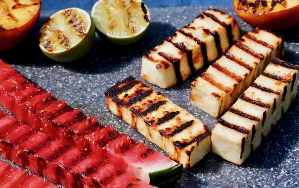 Grilled paneer and fruit on cutting board.