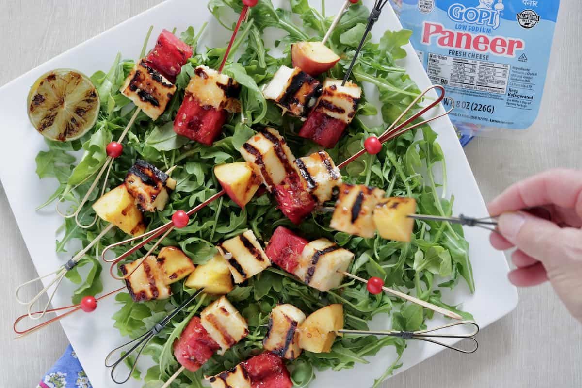 Grilled paneer fruit skewers on a bed of arugula