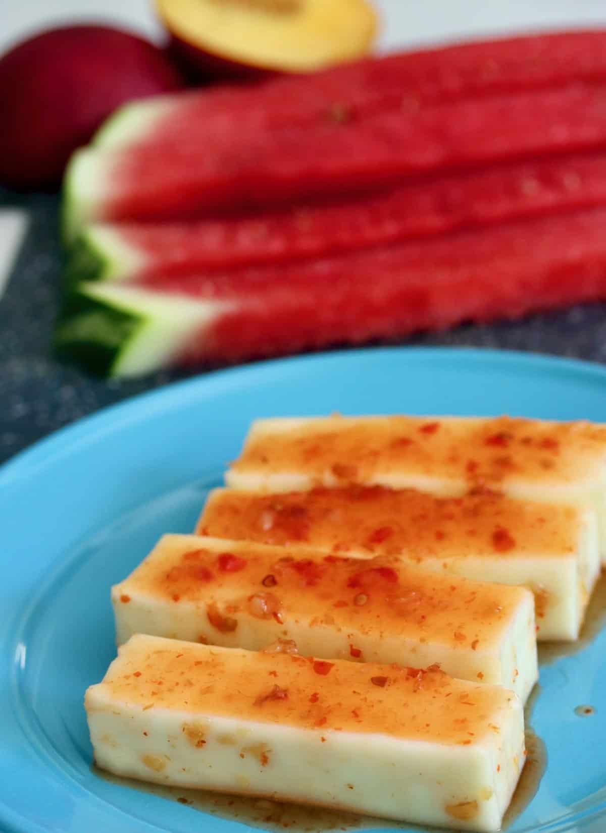 Cut watermelon and paneer marinating in chili sauce on a blue plate.