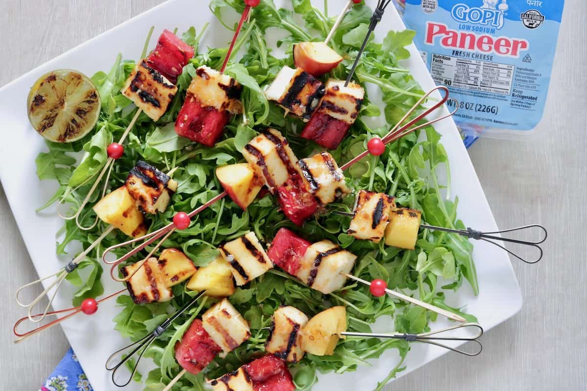 Grilled paneer and fruit skewers on a bed of arugula.