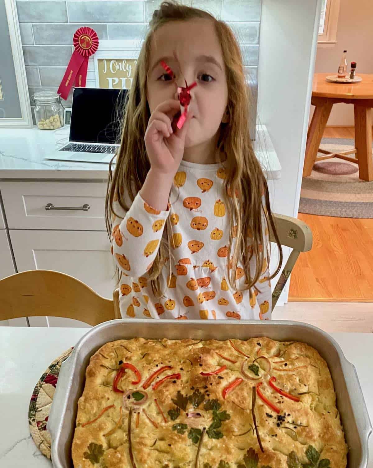 Baked focaccia art bread in pan with my granddaughter blowing a party horn.