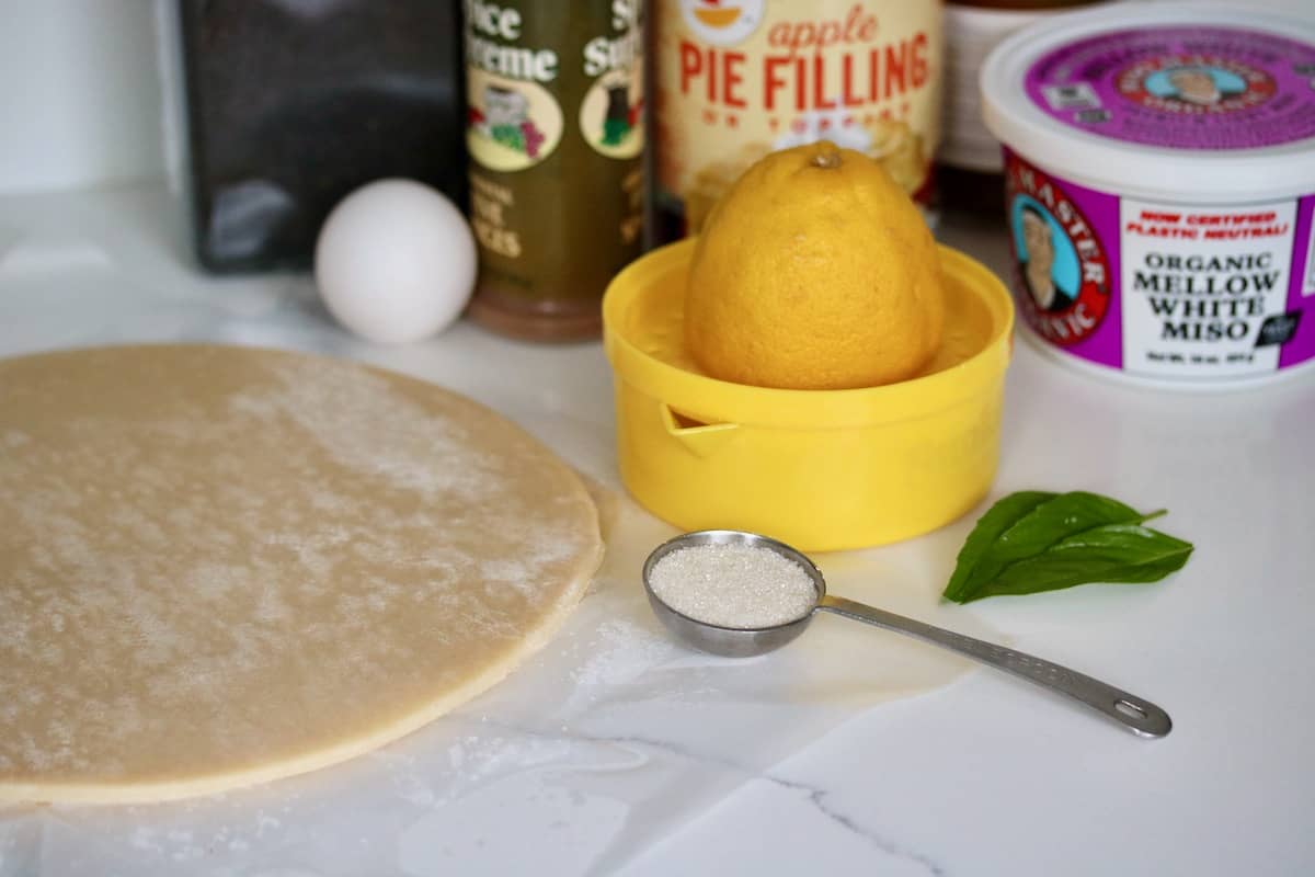 Ingredients for Five-Spice Miso Caramel apple pie with black sesame crust include pie dough, lemon, white miso, sugar, pie filling, caramel, five spice, egg, black sesame seeds.