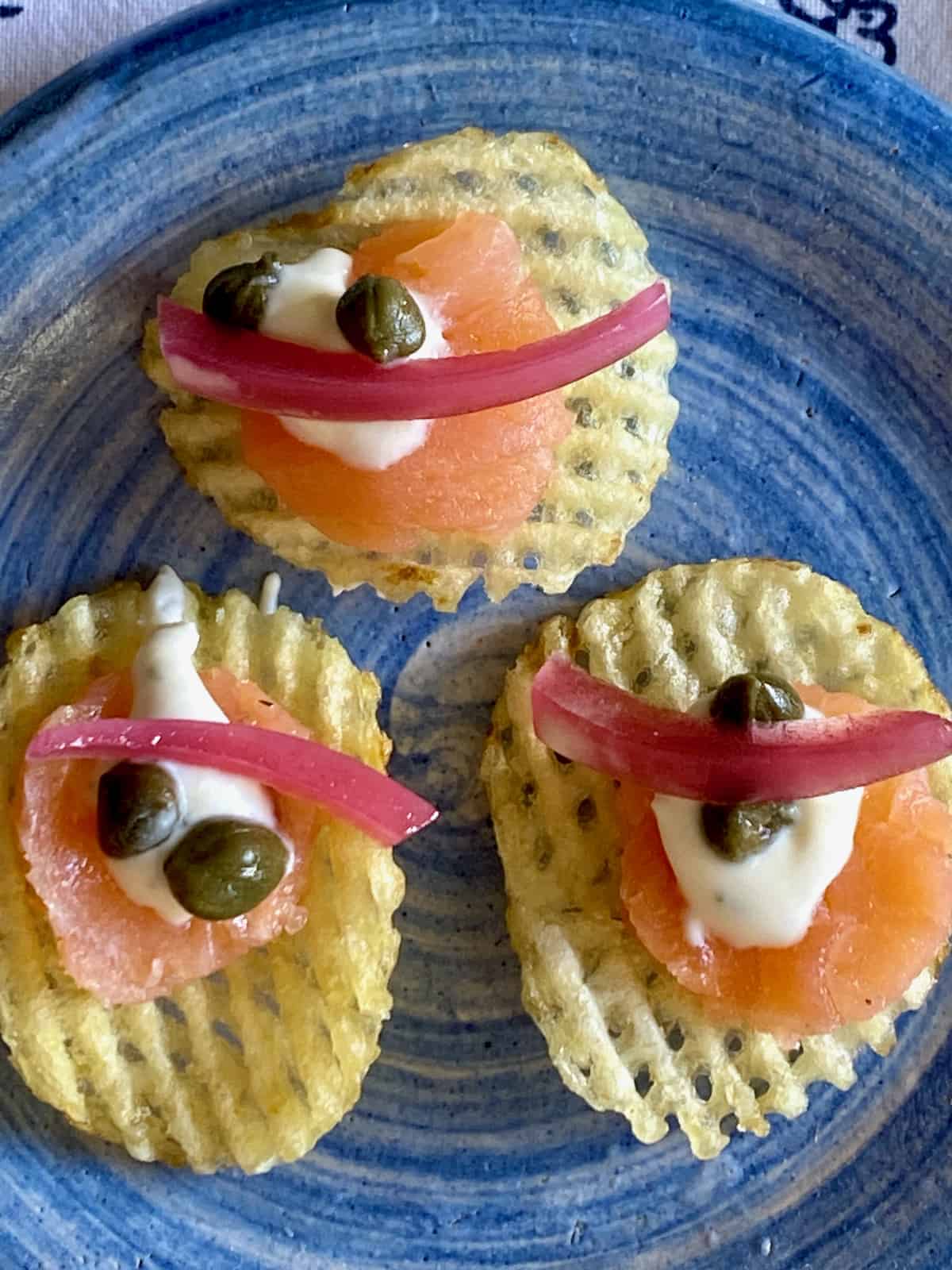 Easy smoked salmon appetizer is salmon on a waffle potato chip with garnishes.