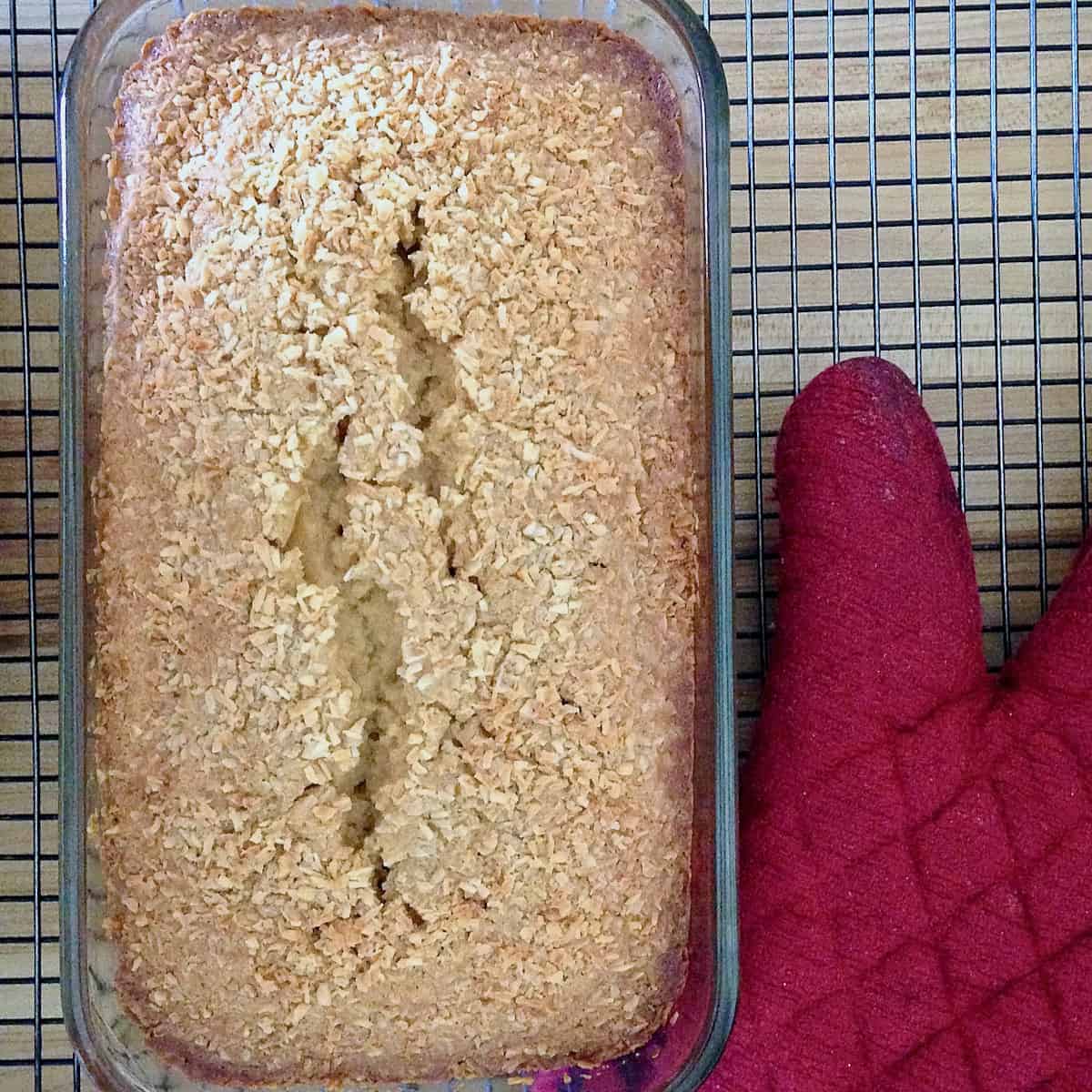 Coconut loaf cake on cooling rack with red potholder.