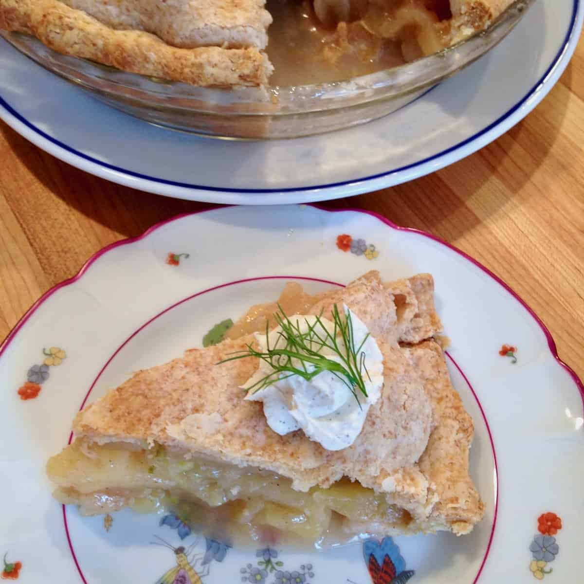 Slice of apple fennel pie topped with cream and fennel frond on a plate.