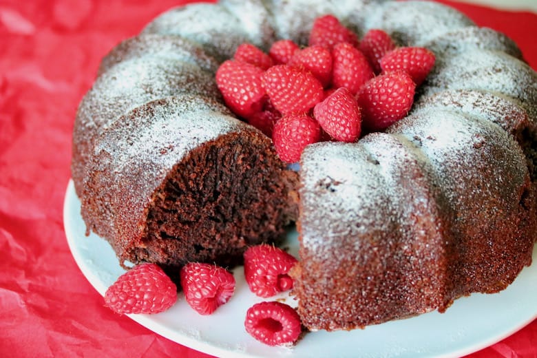 Chocolate raspberry avalanche cake with slice missing and a tumble of raspberries.