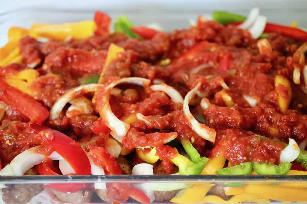 Layers of sausage, peppers, onions and salsa in a baking dish.