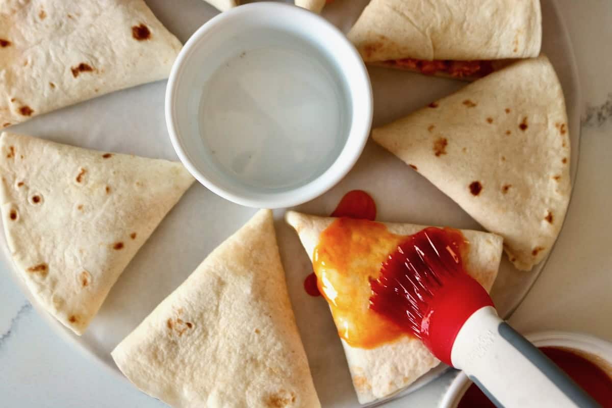 Spreading pepper sauce on quesadillas.