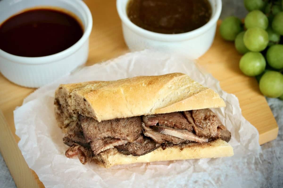 A French dip sandwich and sauce on a cutting board.