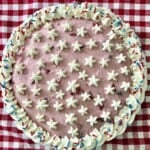 Birthday pie with whipped cream stars and sprinkles on a checkered tablecloth.