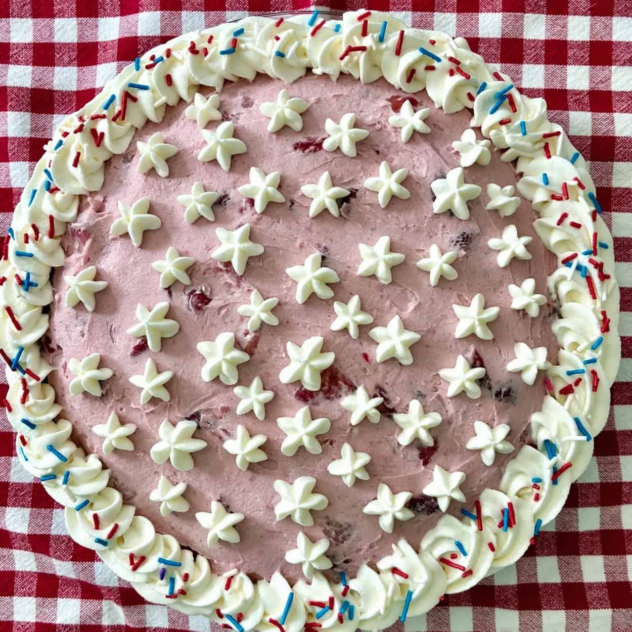 Birthday pie with whipped cream stars and sprinkles on a checkered tablecloth.