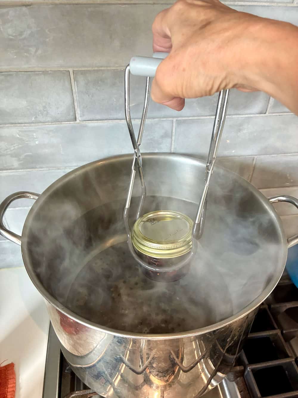 Jar lifter pulling jar from steaming water bath.