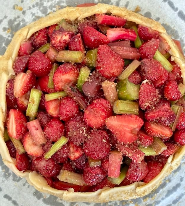 Delicious homemade strawberry rhubarb galette filling with sugar and chopped rhubarb stalks.