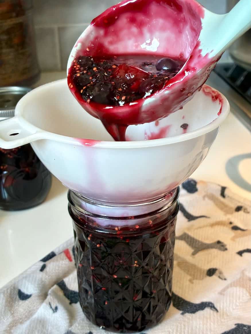 Fresh berry jam being poured through a funnel into a jar.