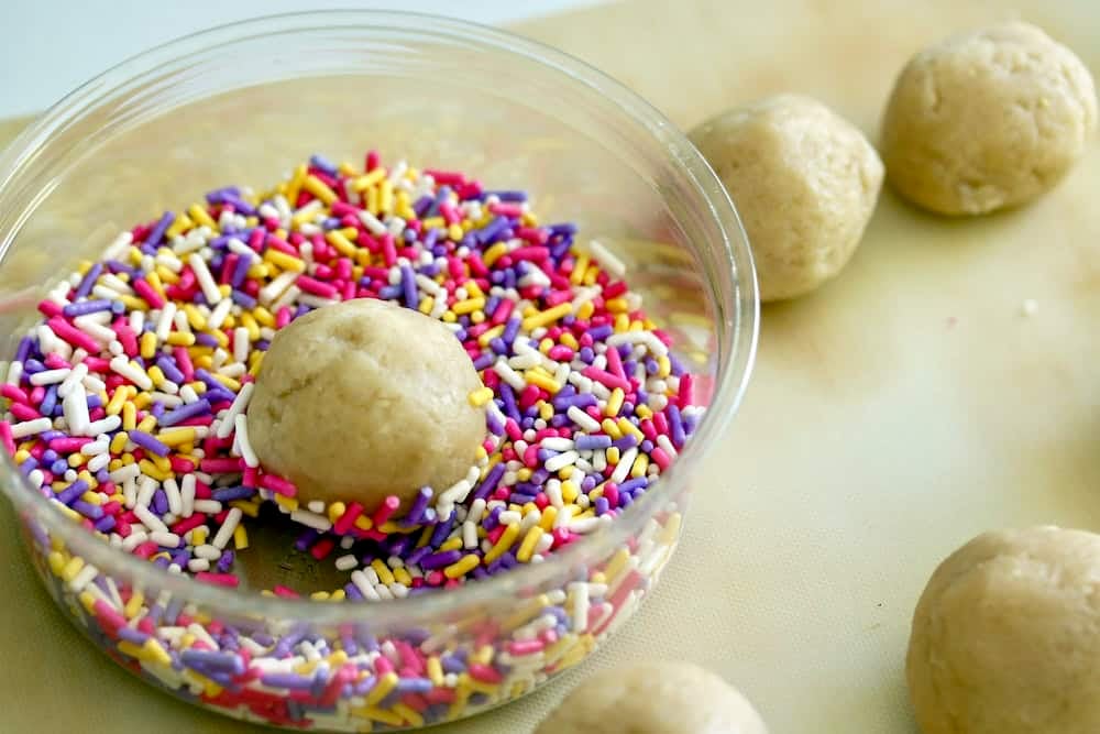 Rolling cookie dough balls in sprinkles.