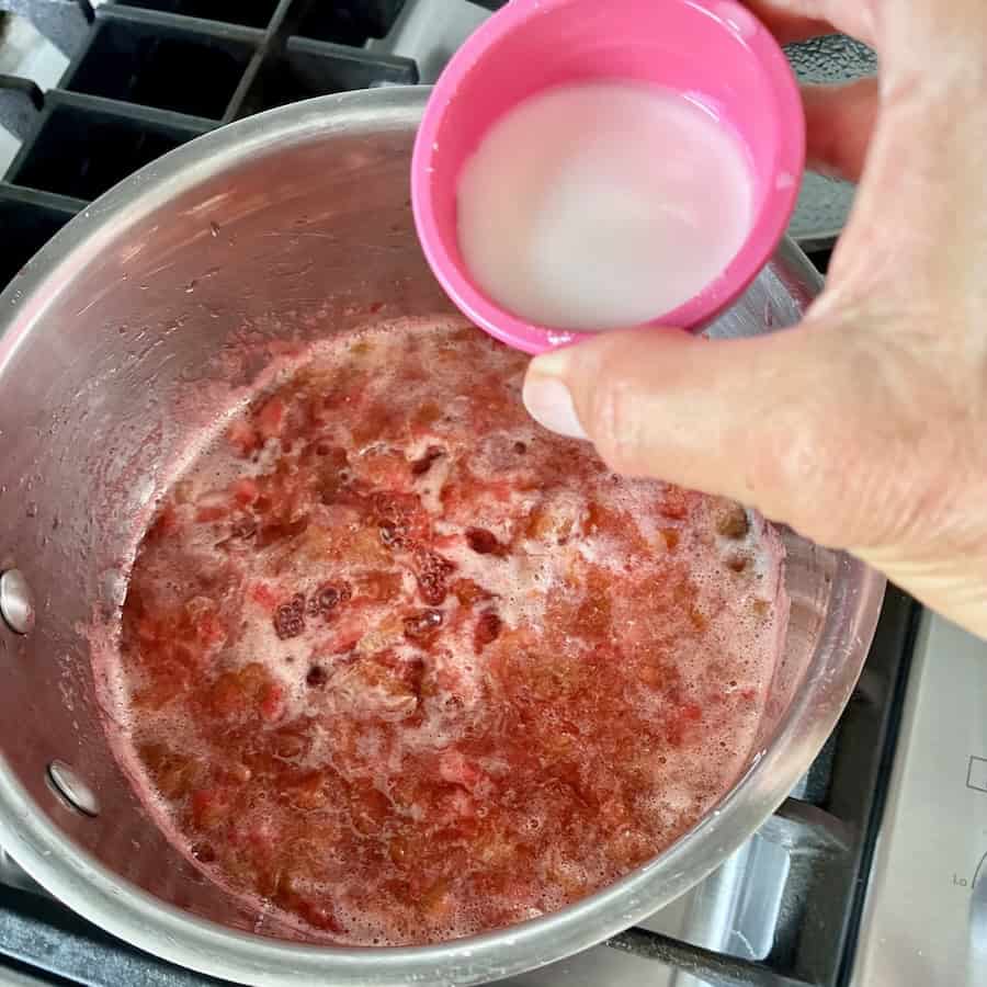 Adding cornstarch slurry to thicken the compote.