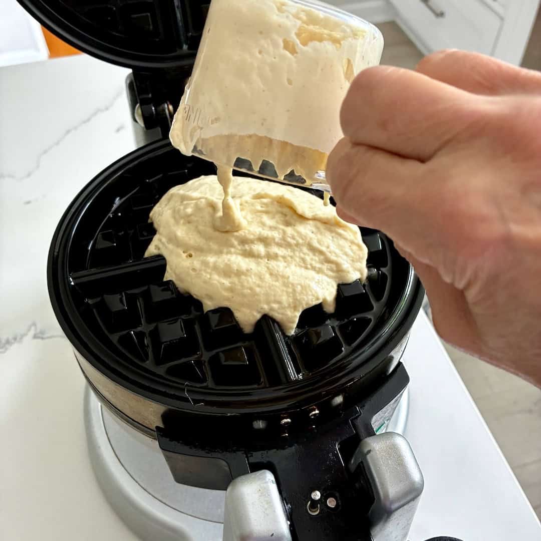 Pouring sourdough waffle batter on waffle iron.