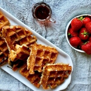 A variety of sourdough discard waffles with strawberries and maple syrup.
