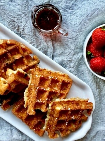 A variety of sourdough discard waffles with strawberries and maple syrup.