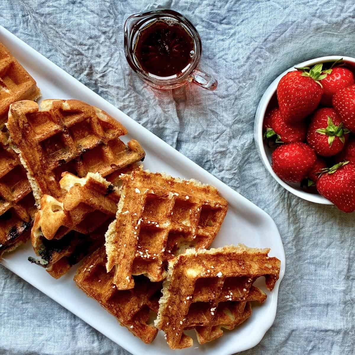 A variety of sourdough discard waffles with strawberries and maple syrup.